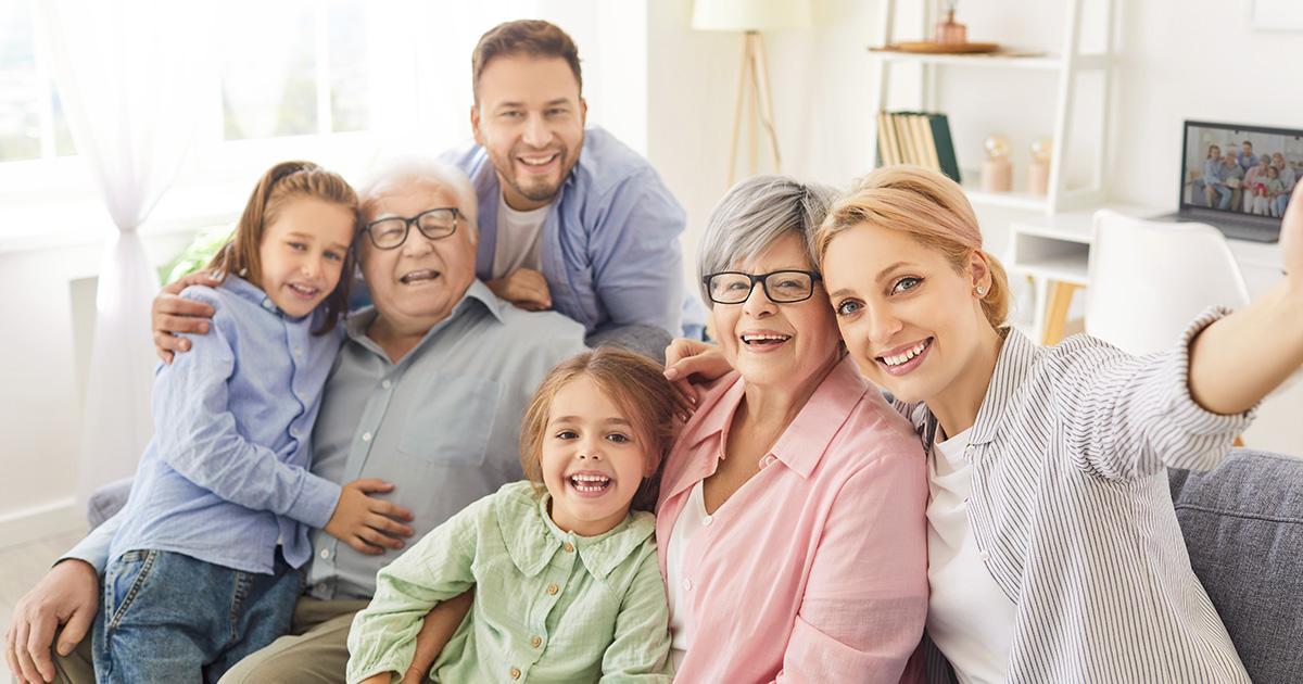 Decorativo. Una familia multigeneracional reunida en y alrededor de un sofá en su casa abraza y sonríe al espectador.