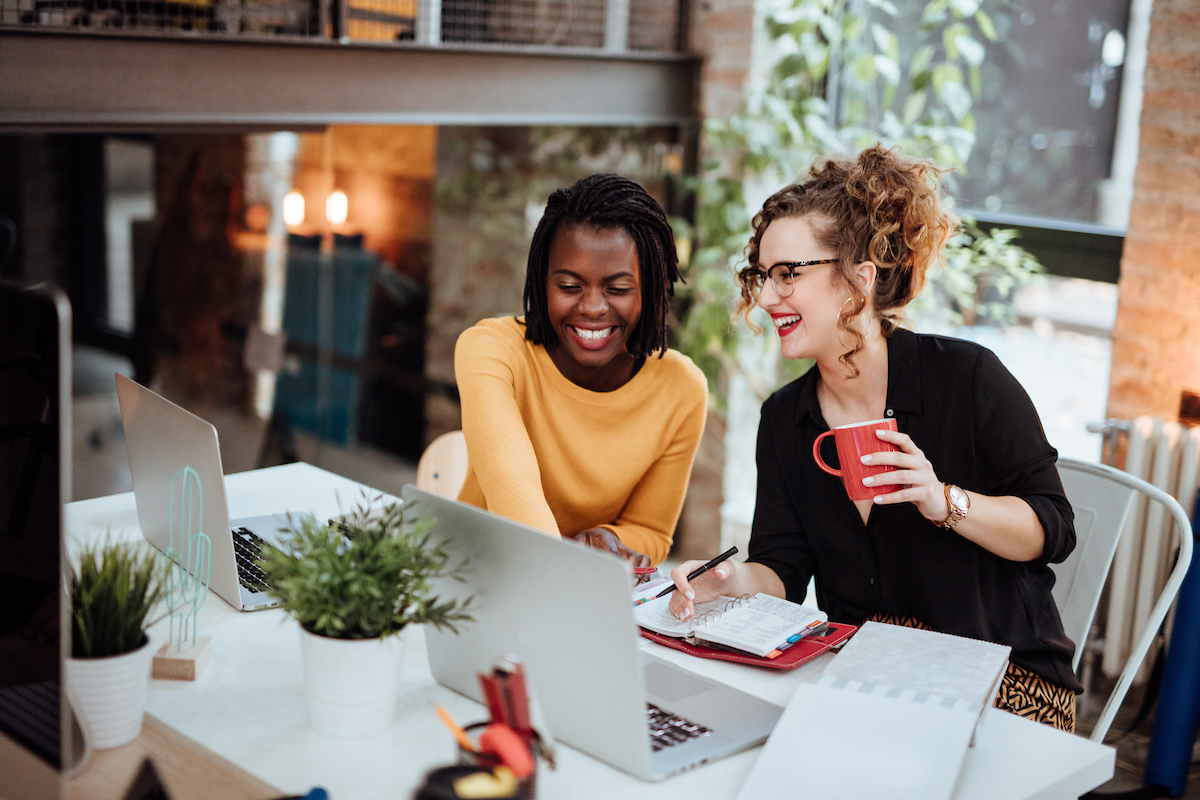 Dos mujeres sentadas en una mesa mirando la pantalla de una computadora portátil.