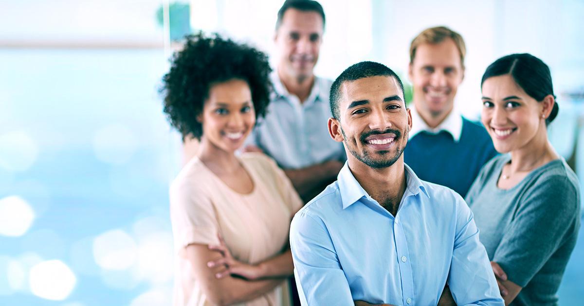 Décoratif. Un groupe diversifié d'employés de bureau en tenue décontractée se tient debout en groupe serré. Ils ont les bras croisés et sourient au spectateur. Une série de fenêtres floues se trouve à l'arrière-plan.