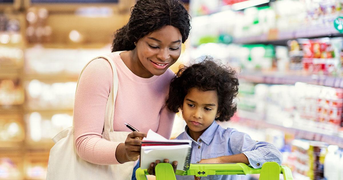 Décoratif. Une mère et son enfant font leurs courses dans une épicerie, en poussant un chariot. La mère sourit et montre à l'enfant comment utiliser une liste de courses écrite dans un cahier.