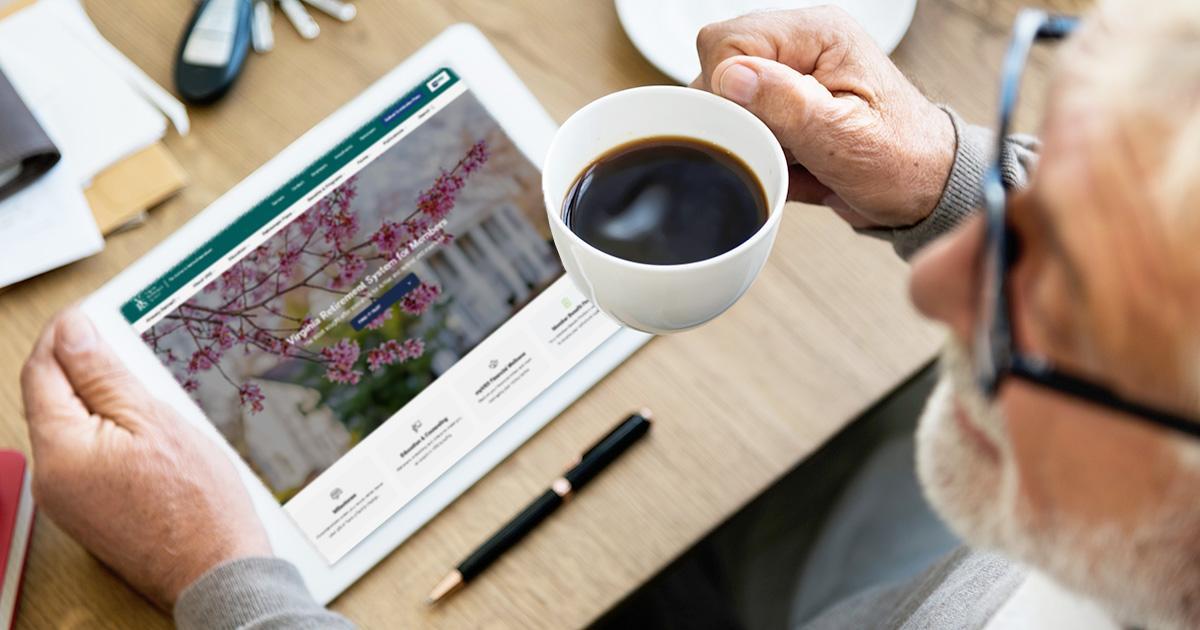 Décoratif. Vue de dessus d'un homme d'âge mûr assis à une table dans un café. Il tient une tasse de café noir dans sa main droite tout en consultant le site web VRS sur sa tablette informatique posée sur la table.