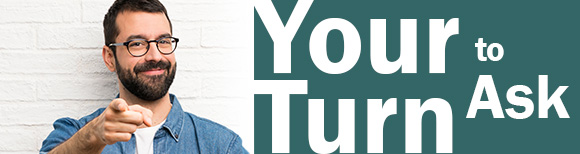 안경을 쓴 수염 난 남성이 미소를 지으며 자신의 차례를 읽고 있는 텍스트 옆의 시청자를 가리키며 묻습니다.