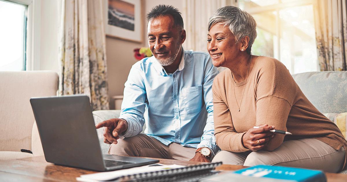 Decorative. Photo of a smiling couple seated on a couch with a laptop computer on the coffee table in front of them.