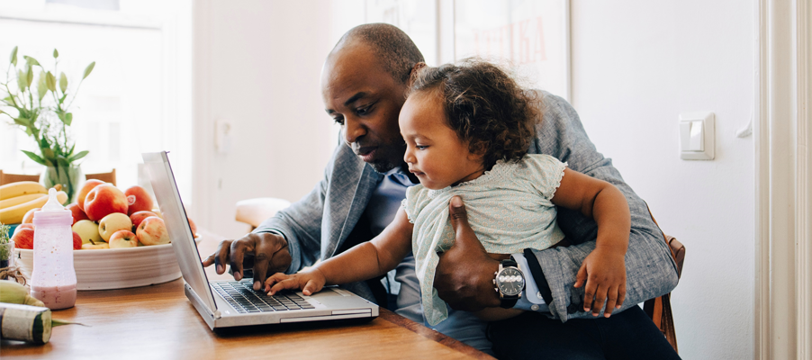A person holding a baby while using a computer.