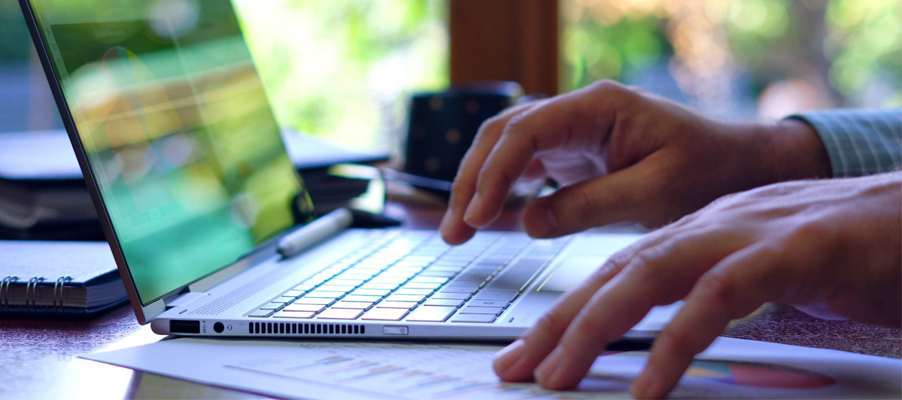 Hands typing on a laptop keyboard with a blurred computer screen in the background.