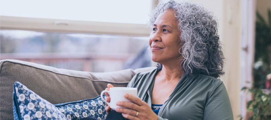 Person sitting by a window holding a mug and looking outside.