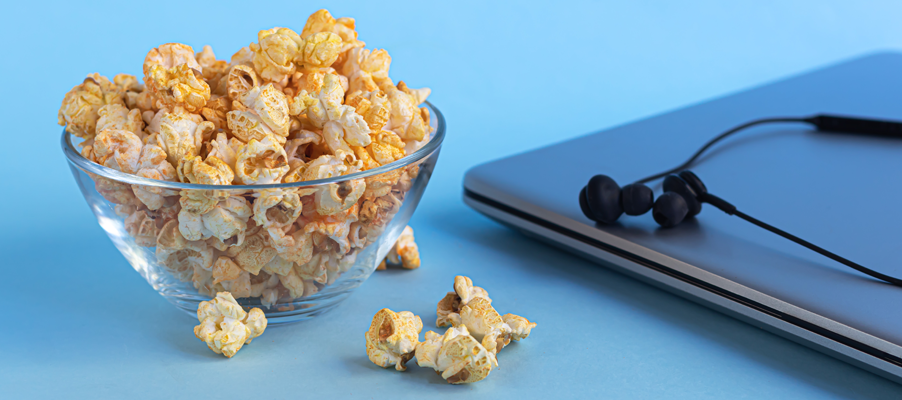 Bowl of popcorn beside a tablet and earphones on a blue surface.