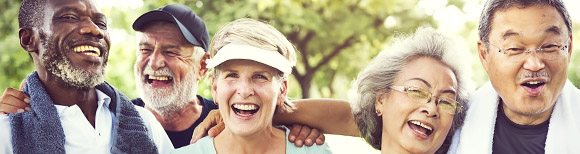 Decorative. Five adults near retirement age wearing weekend attire smile and laugh while enjoying one another's company. Trees are in the background.
