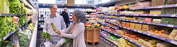 A man and a woman select a bunch of asparagus in the produce department of a grocery store.