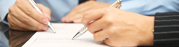 hands of two people holding pens and signing paperwork