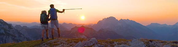 装饰性一男一女身着远足装备，站在岩石山坡上。在他们面前的是一座座山脉。太阳低垂在地平线上。